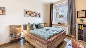 A bedroom with a wooden bed, a nightstand, a window with curtains, and a bookshelf.