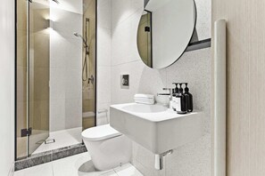 A modern bathroom with a glass-enclosed shower, a white sink with toiletries, and a large mirror. - Luxury Stay Near Grand Prix Track (Melbourne)