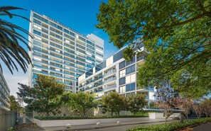 A modern multi-story building with balconies, surrounded by greenery and a clear sky. - Luxury Stay Near Grand Prix Track (Melbourne)