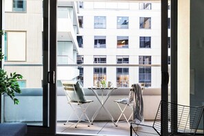 A balcony with a table and chairs, a potted plant, and a view of a multi-story building. - Luxury Stay Near Grand Prix Track (Melbourne)