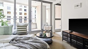 A modern bedroom with a large window, a bed, a round coffee table, a TV, and a balcony. - Luxury Stay Near Grand Prix Track (Melbourne)