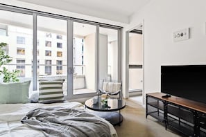 A modern bedroom with a large window, a bed, a round coffee table, a TV, and a balcony. - Luxury Stay Near Grand Prix Track (Melbourne)