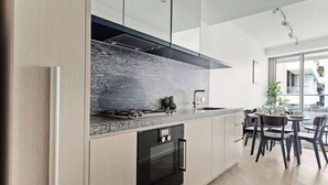 A modern kitchen with a granite countertop, stainless steel appliances, and a dining area with a round table and chairs. - Luxury Stay Near Grand Prix Track (Melbourne)