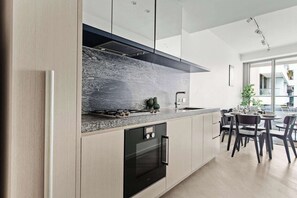 A modern kitchen with a granite countertop, stainless steel appliances, and a dining area with a round table and chairs. - Luxury Stay Near Grand Prix Track (Melbourne)