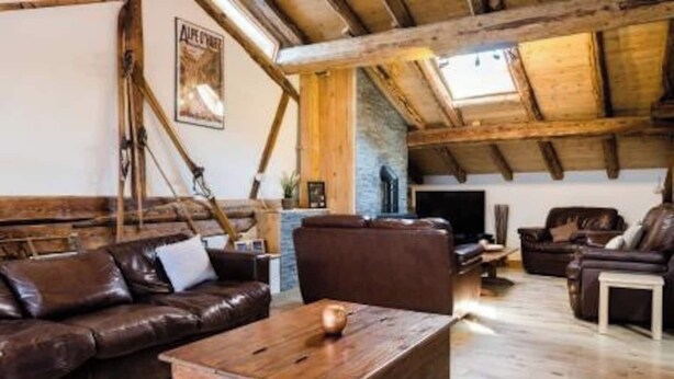 A rustic living room with wooden beams, a brown leather sofa, a wooden coffee table, and a stone fireplace. - Chalet Bronziers - authentic alpine experience (10p, sauna) (Peisey-Nancroix)