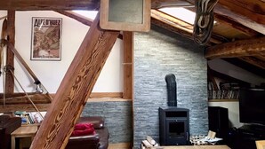 A rustic attic room with exposed wooden beams, a stone wall, a fireplace, and a framed poster. - Chalet Bronziers - authentic alpine experience (10p, sauna) (Peisey-Nancroix)