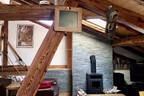 Une chambre mansardée au charme rustique, avec des poutres apparentes, un mur en pierre, une cheminée et une affiche encadrée.