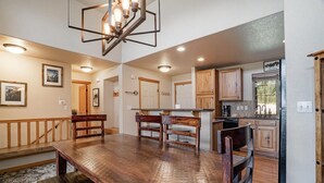 A spacious dining area with a wooden table and benches, a kitchen with wooden cabinets, and a chandelier. - 177 Wildflower - Mountain Home with New Hot Tub (Fraser)