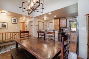 A spacious dining area with a wooden table and benches, a kitchen with wooden cabinets, and a chandelier.