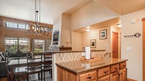 A spacious kitchen with wooden cabinetry, a granite countertop, and a dining area with a table and chairs. - 177 Wildflower - Mountain Home with New Hot Tub (Fraser)