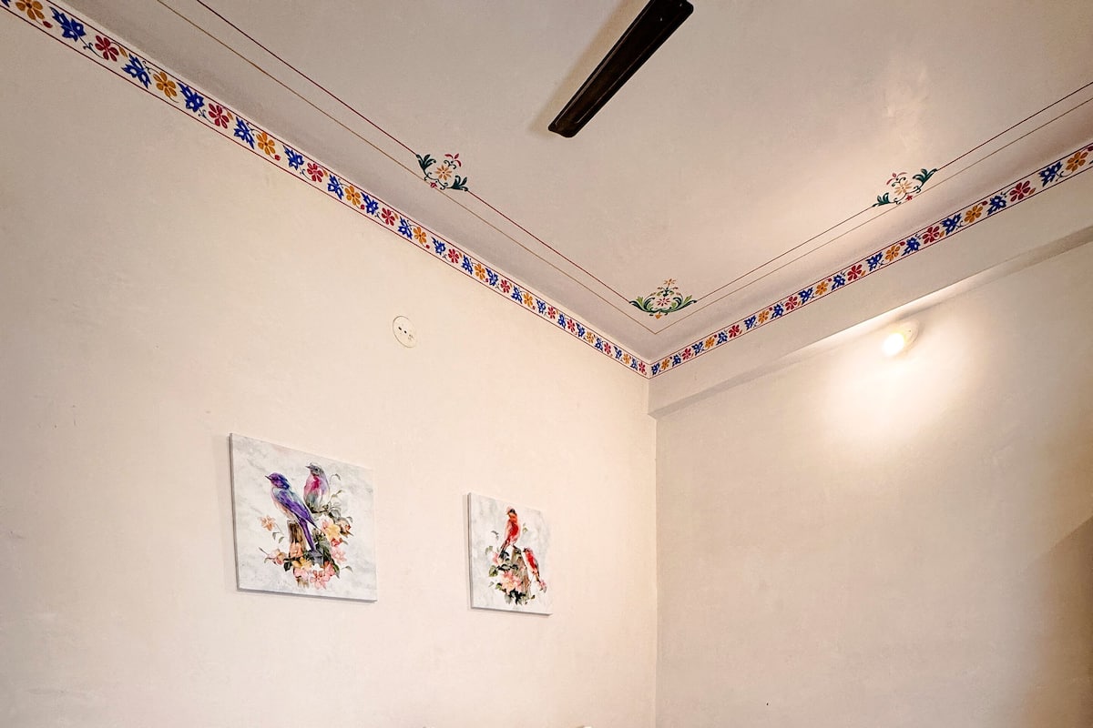 A hotel room with a bed, pillows, a blanket, a quilted throw, a remote control, and two wall-mounted paintings.