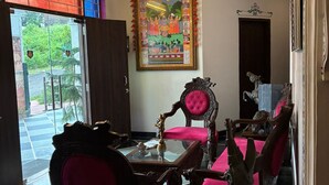 A room with a chandelier, a large framed painting, and a door with a number sign. - Hotel Kanak Niwas (Udaipur)