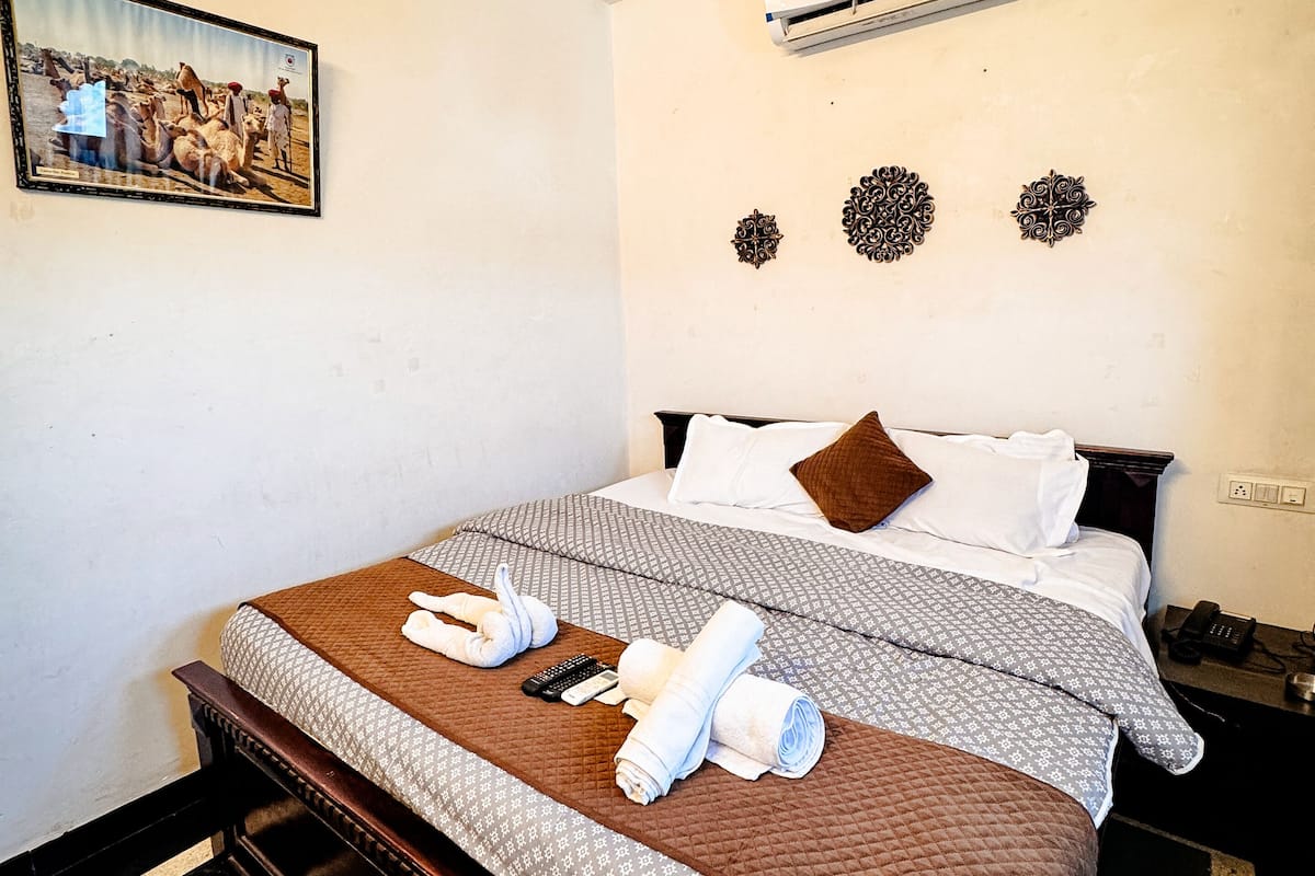 A hotel room with a bed, a picture on the wall, an air conditioner, and decorative wall pieces.
