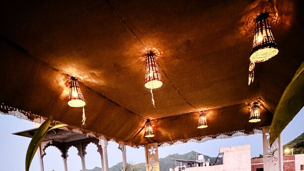 An outdoor seating area with patterned cushions, potted plants, and hanging lights. - Hotel Kanak Niwas (Udaipur)