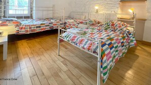 Een slaapzaal met drie stapelbedden, houten vloer, witte muren en een accentmuur van steen.