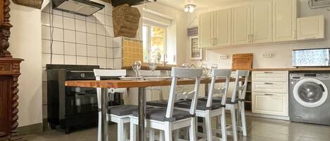 A kitchen with a dining table, chairs, a washing machine, and a stove.
