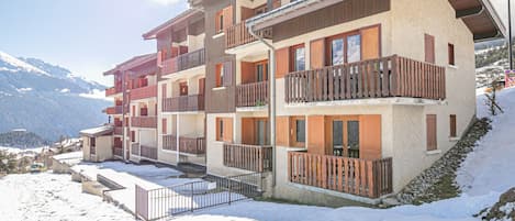 A multi-story hotel with balconies and a ski slope in the background.