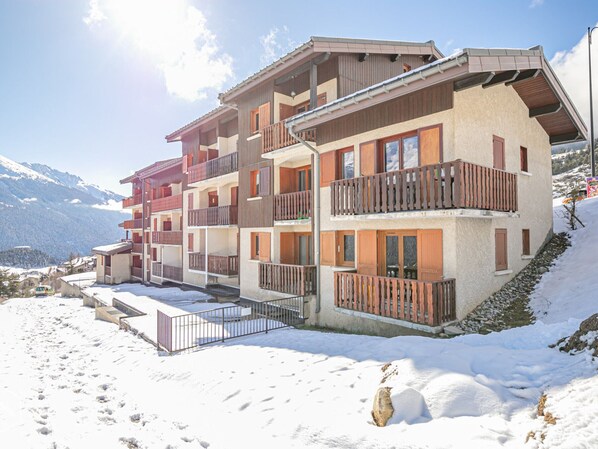 A multi-story hotel with balconies and a ski slope in the background.
