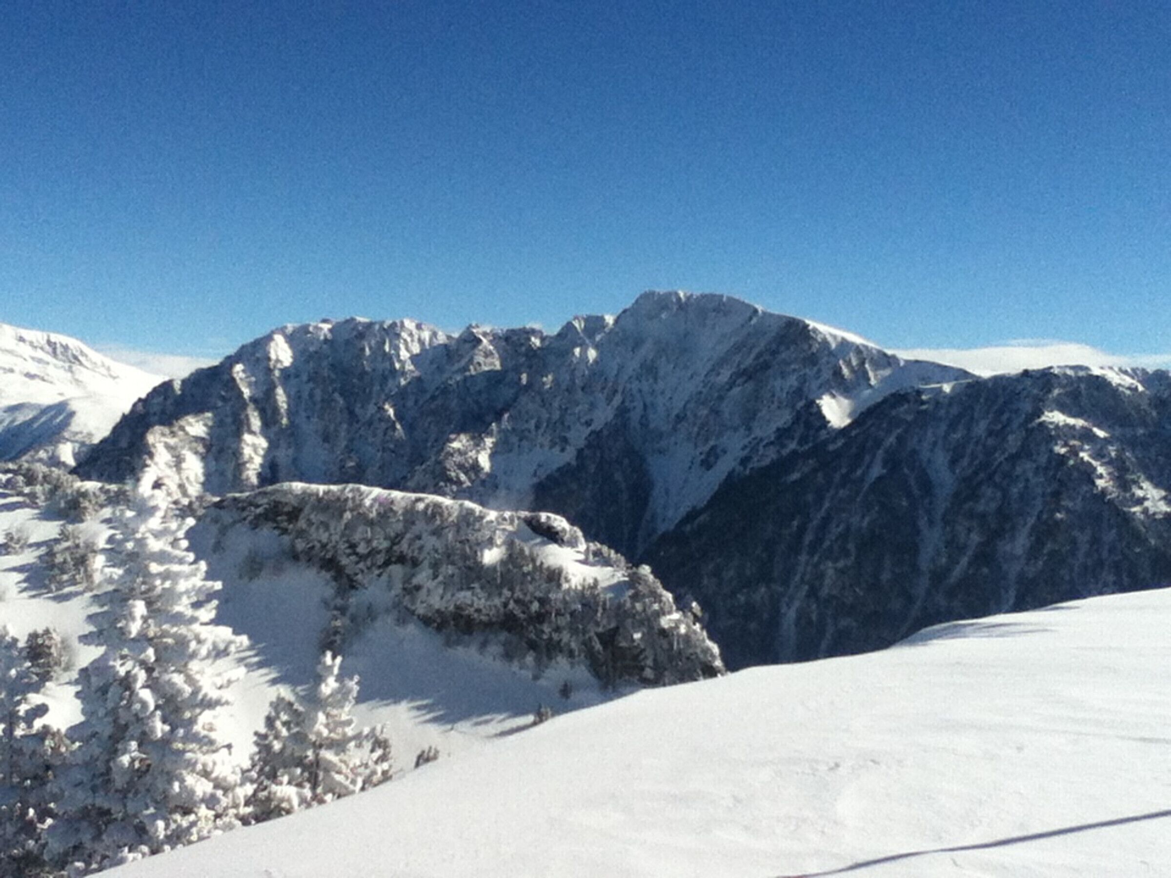 A snow-covered mountain landscape with rocky peaks and sparse trees.
