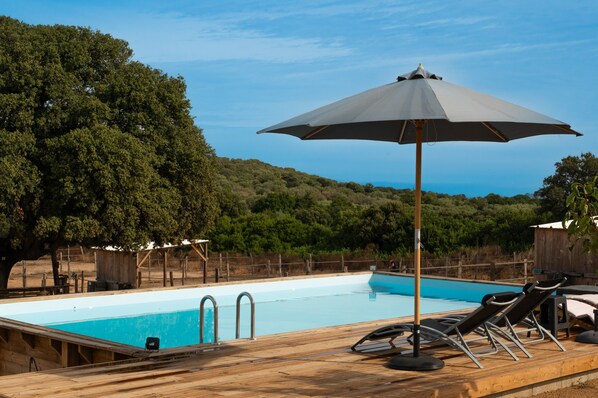 A swimming pool with lounge chairs and an umbrella, surrounded by trees and hills.