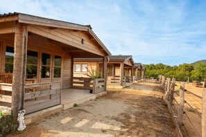 A row of wooden cabins with covered porches, a gravel path, and a fenced area.