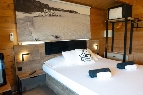 Une chambre d’hôtel avec un lit, une table de chevet, une télécommande, un téléviseur fixé au mur et un tableau représentant un paysage enneigé.