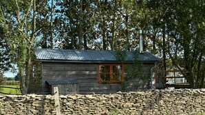 Une cabane rustique avec un mur en pierre, une fenêtre rouge et un toit en métal.