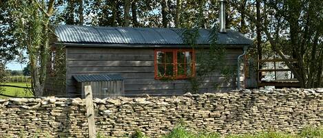 A rustic cabin with a stone wall, a red window, and a metal roof.