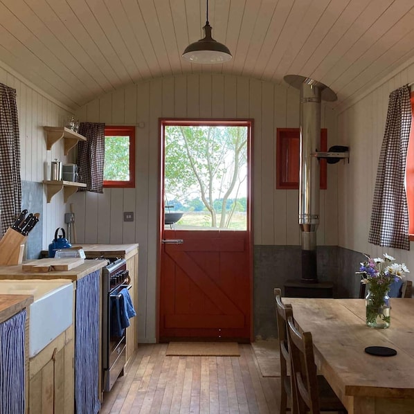 A rustic kitchen with wooden walls, a red door, and a view of greenery outside.