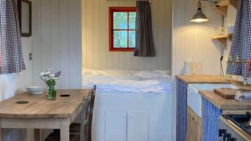 A compact room with a bed, a small table with a vase of flowers, a kitchenette with a sink and stove, and a window with curtains.