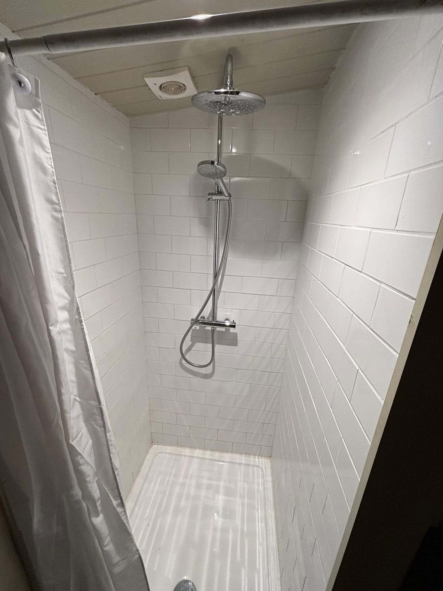 A small, tiled shower area with a showerhead and handheld shower attachment.
