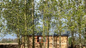Une petite cabane en bois avec une porte rouge, entourée d’une clôture en bois et d’arbres.