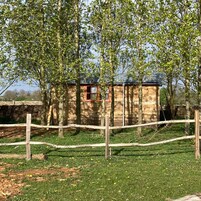 A small wooden cabin with a red door, surrounded by a wooden fence and trees.