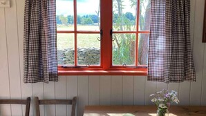 Une pièce avec une table en bois, deux chaises, une fenêtre avec un encadrement rouge et des rideaux à carreaux.