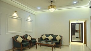A living room with a green sofa set, two armchairs, a coffee table, and a chandelier. - Family Ties Homestay (Varanasi)
