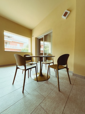 A dining area with a round table and four chairs, large windows, and a view of buildings outside.