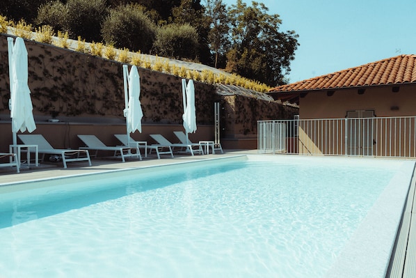 A swimming pool with lounge chairs and umbrellas, a tiled roof, and a wall with climbing plants.