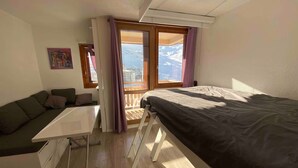 A compact room with a bed, a small sofa, a desk, and a window with a view of mountains. - Ski in, ski out APPT in the resort center (Les Belleville)