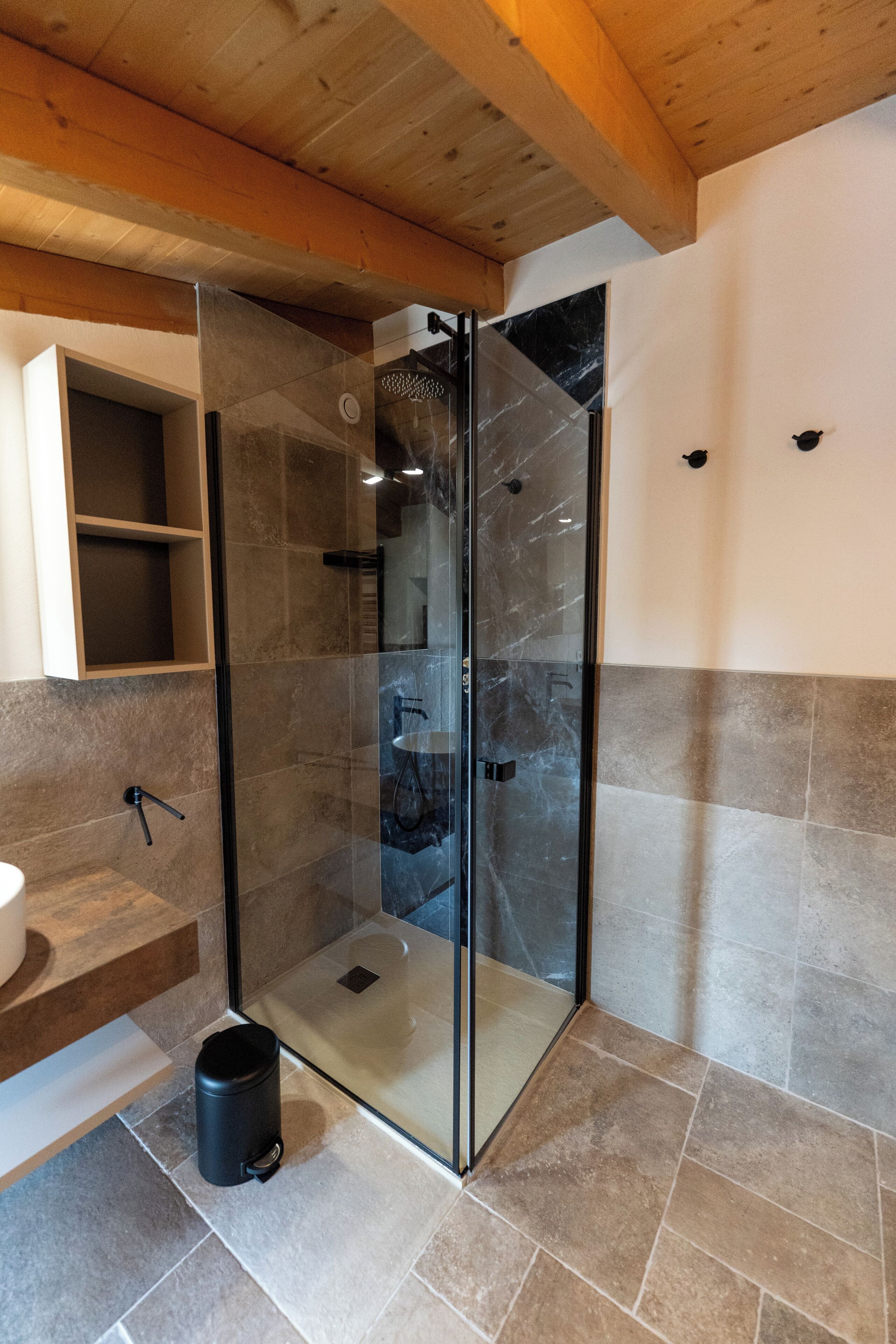 A modern bathroom with a glass shower enclosure, a wooden ceiling, and a marble-tiled floor.