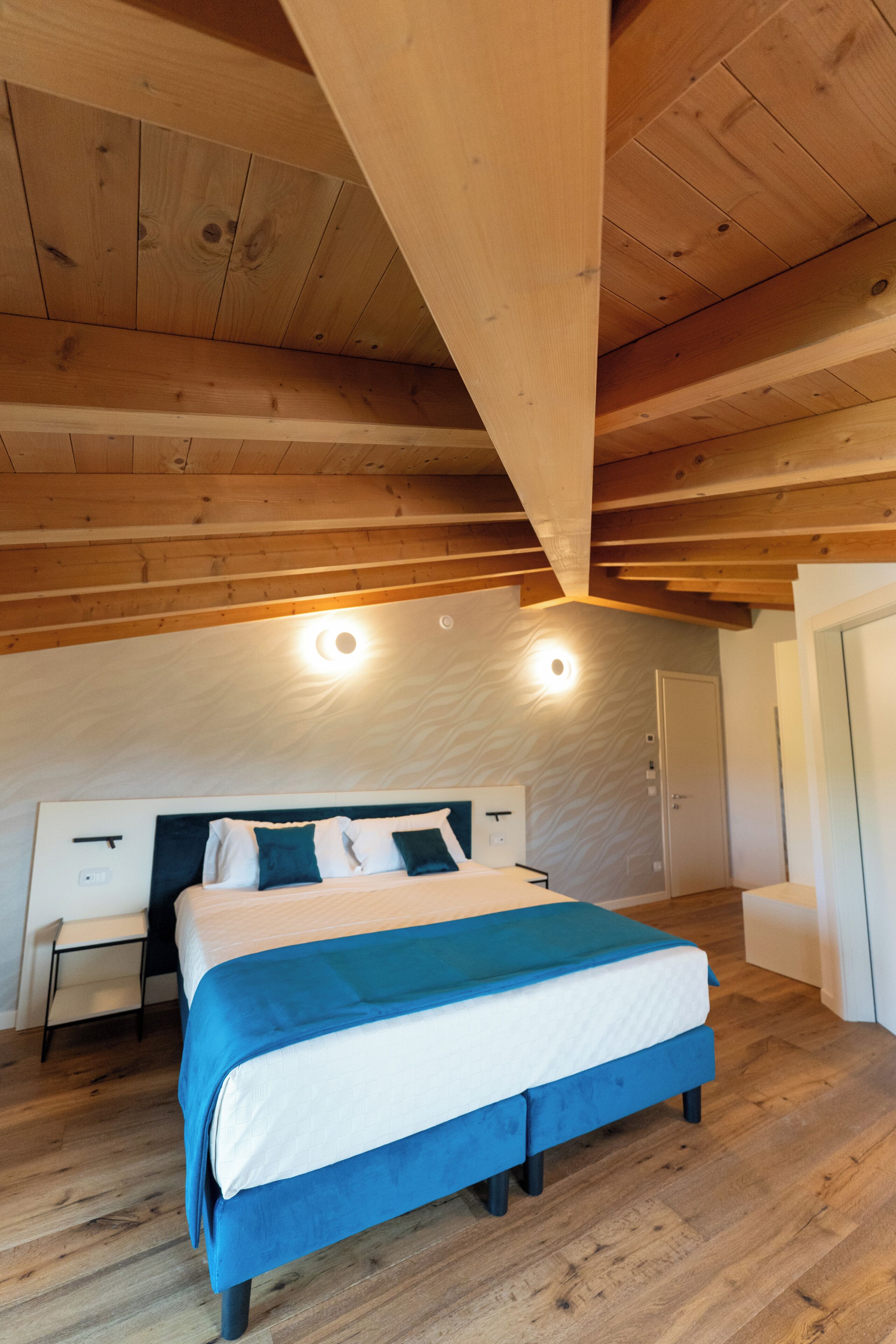 Ein Schlafzimmer mit Holzboden, einem Bett mit blauer und weißer Bettdecke, einem Nachttisch und einer Tür.