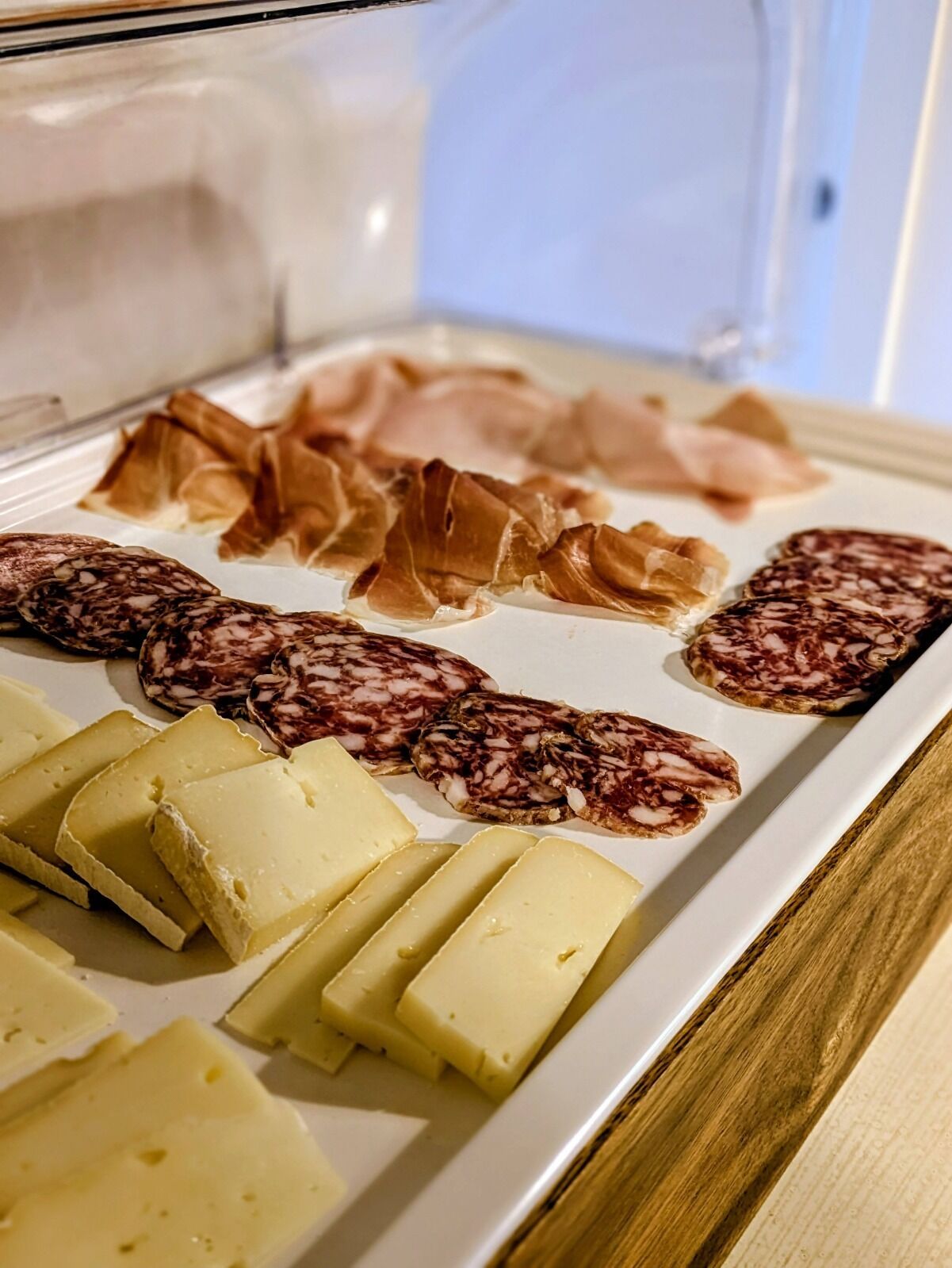 A display of various cheeses and cured meats in a refrigerated case.