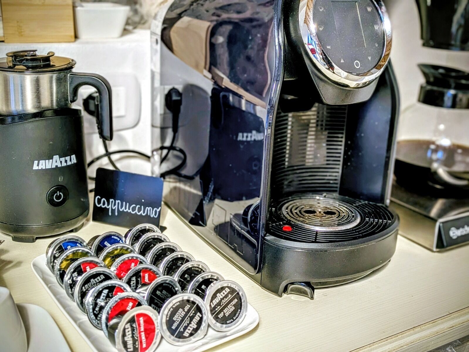 Eine Kaffeemaschine, eine Kaffeekanne und eine Auswahl an Kaffeekapseln auf einer Arbeitsfläche.