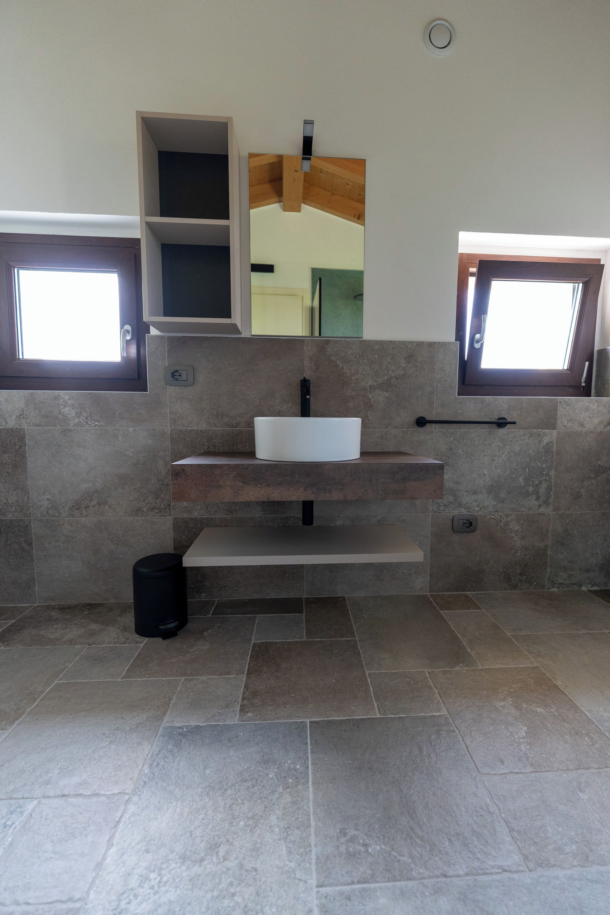 A modern bathroom with a built-in sink, a mirror above it, and a window on the left side.