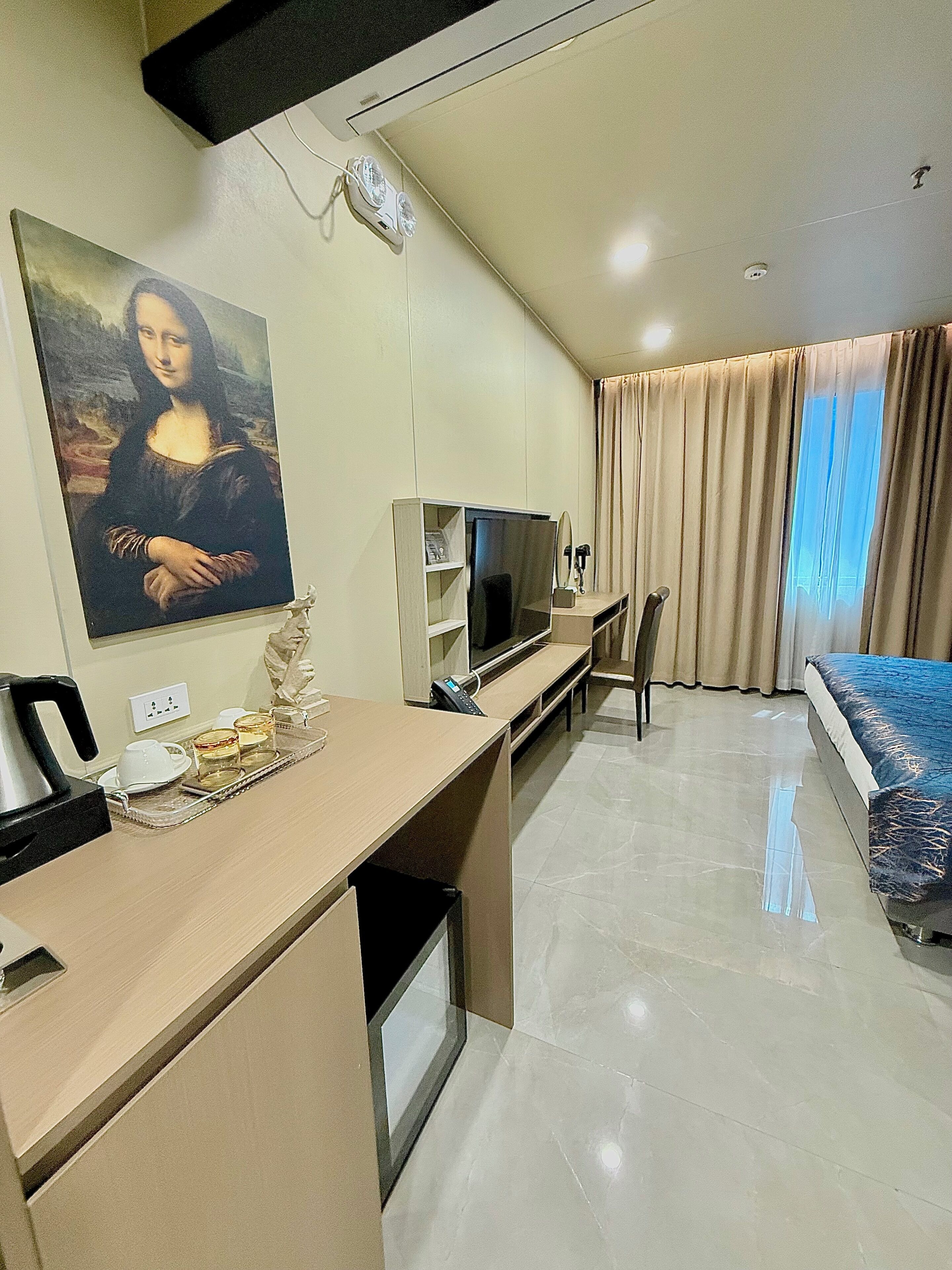 Habitación de hotel con televisión de pantalla plana, escritorio con teléfono, cafetera y bandeja con tazas y vasos.
