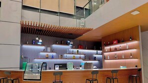 Un área de bar moderna con mostrador de madera, taburetes y estanterías con botellas.