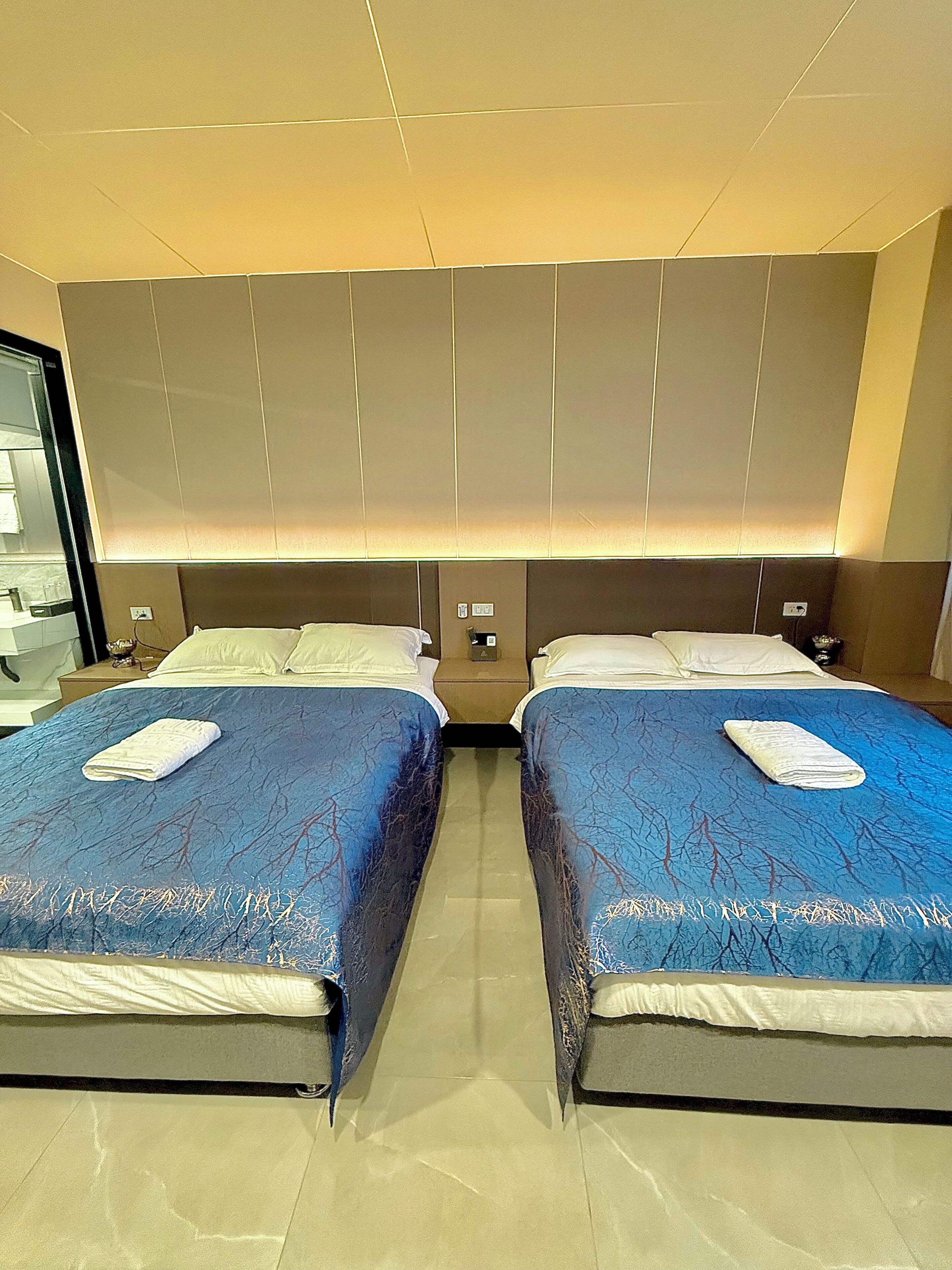 A hotel room with two beds, a large mirror, and a modern light fixture above the beds.