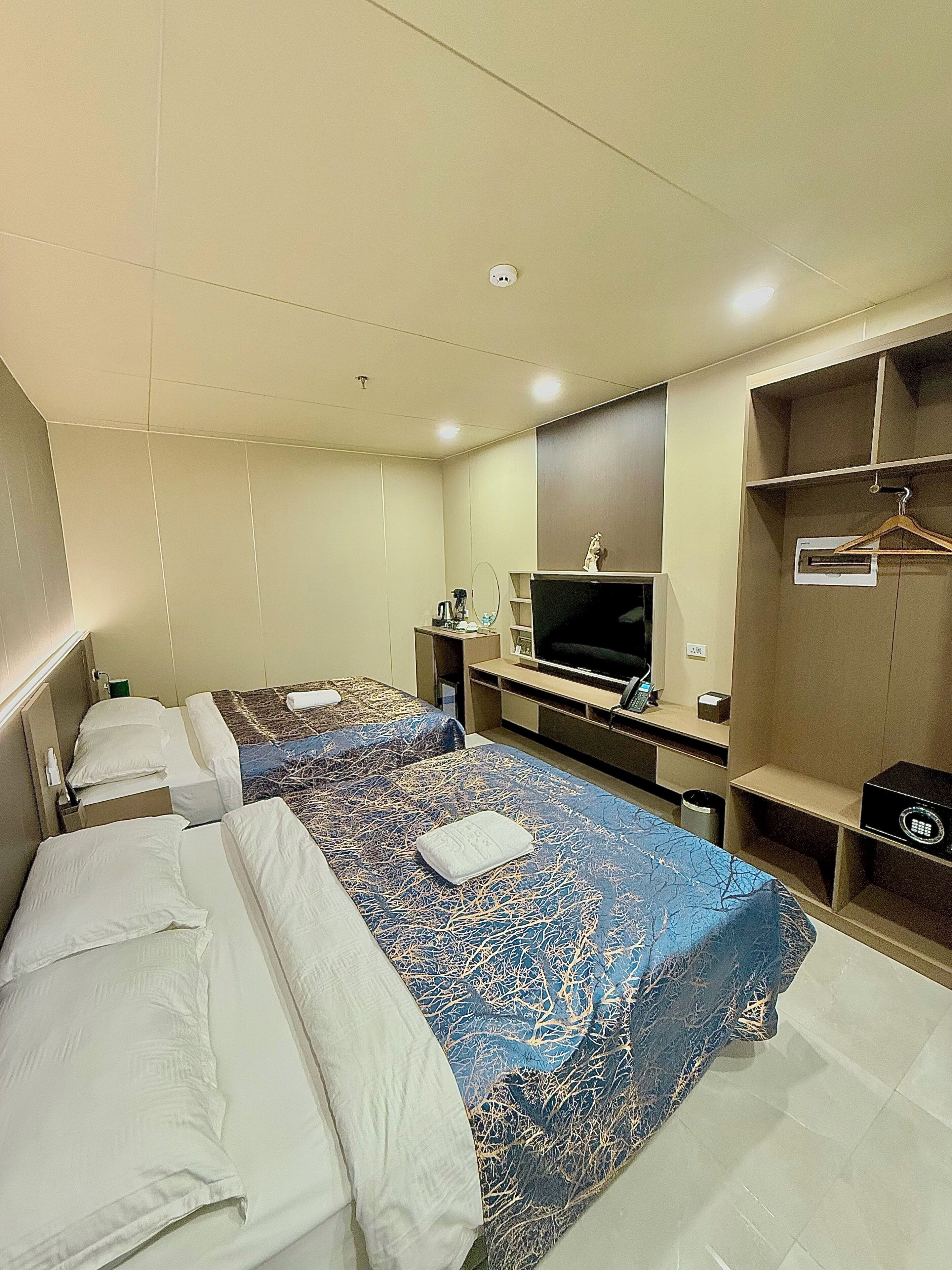 A hotel room with two beds, a TV, a wardrobe, and a desk with a chair.
