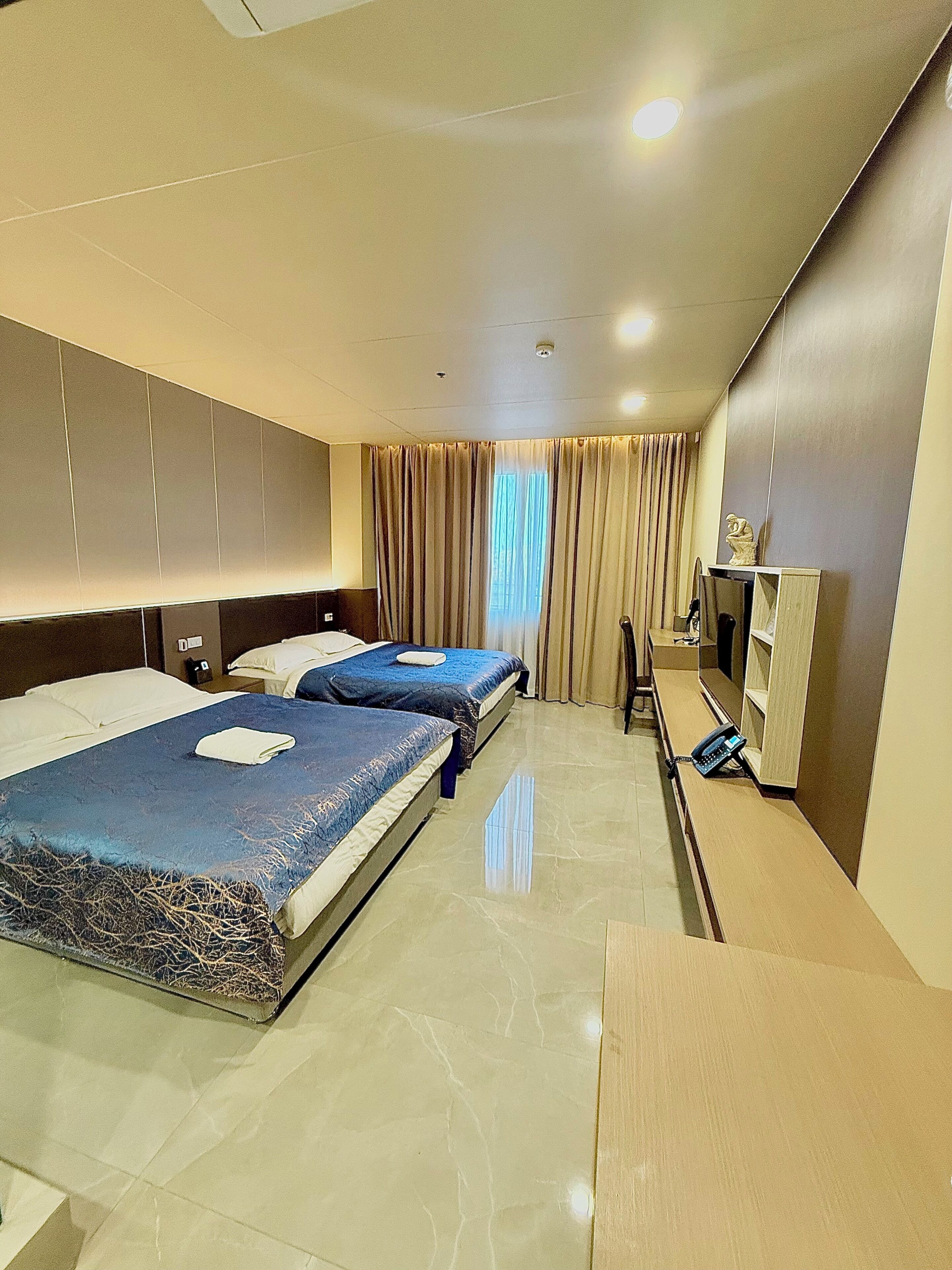 A hotel room with two beds, a desk, a telephone, and a television.