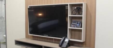 A modern living room with a flat-screen TV, a telephone, and a small shelf with items.