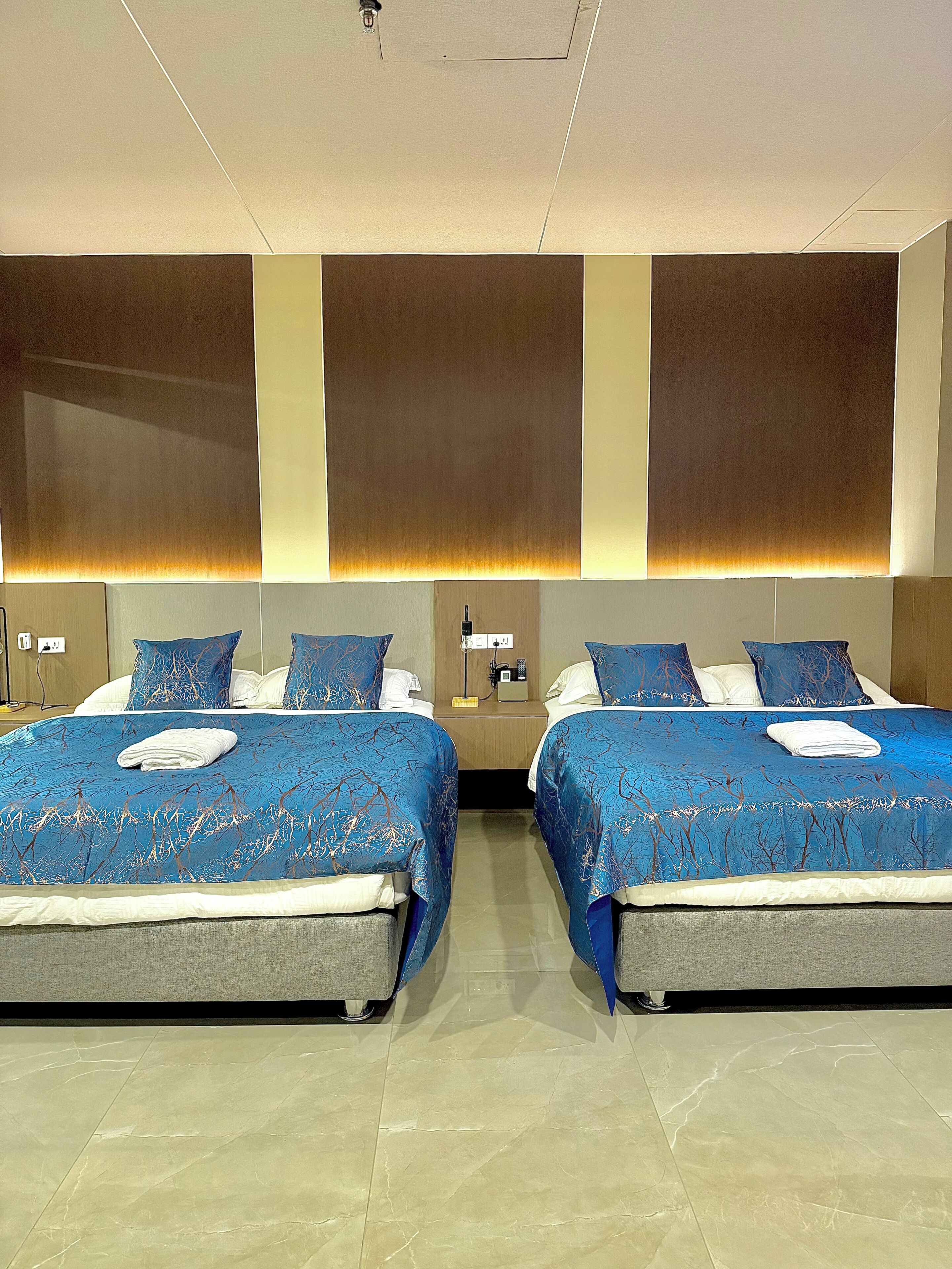 A hotel room with two beds, a nightstand, and a wall-mounted lamp.